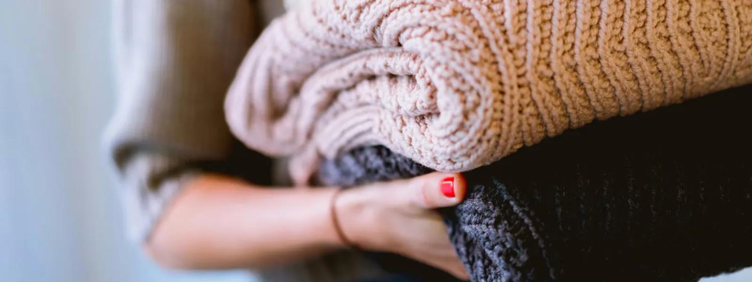 Woman holding beige and black knitted sweaters.